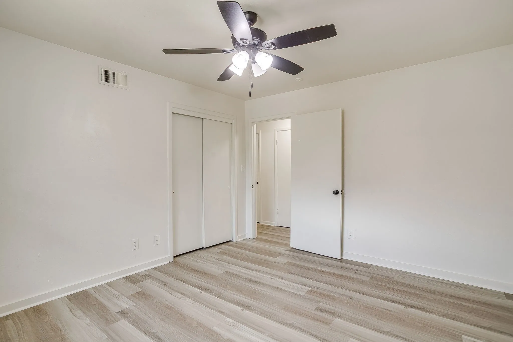 Spacious room featuring wood-finish flooring, white walls, and a ceiling fan with integrated lighting