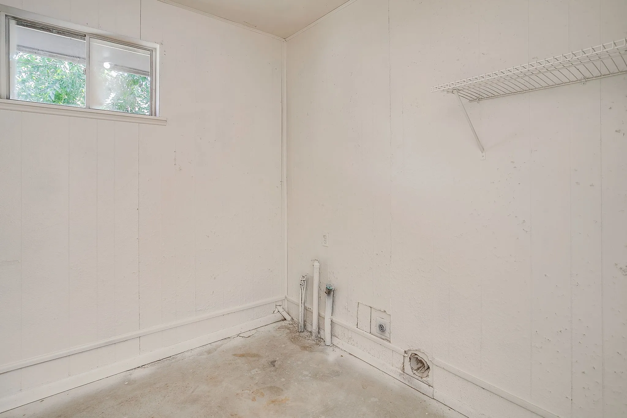 Utility space featuring a single window, white paneling, and a wire shelf