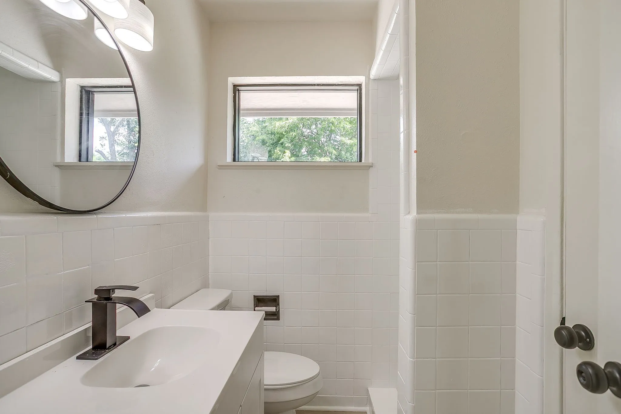 Bathroom featuring a vanity with an integrated sink, matte black faucet, and a round mirror