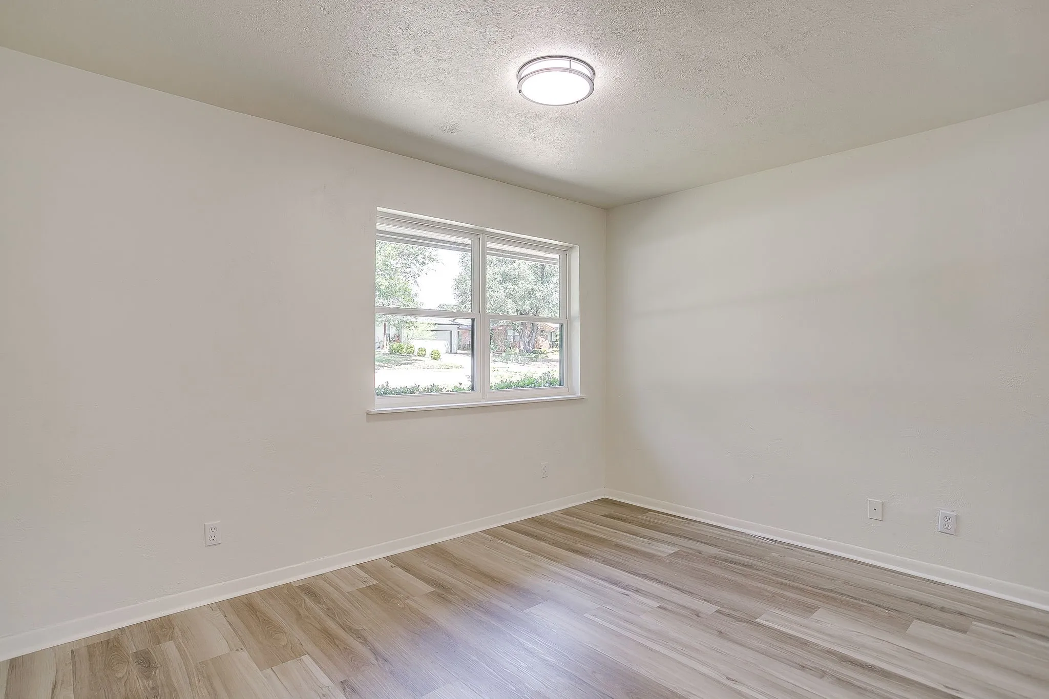 Bright interior space featuring a window with white trim, wood-finish flooring, white baseboards, and a contemporary ceiling light fixture