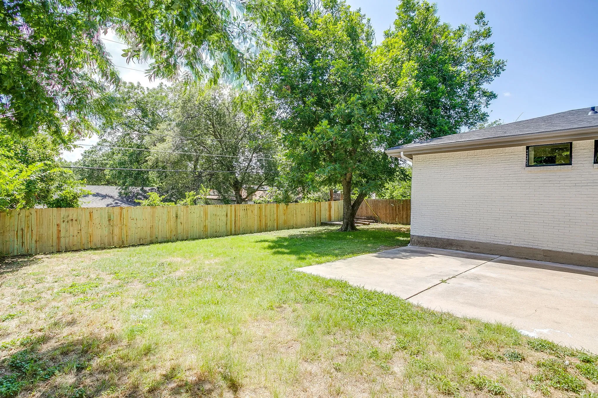 Expansive grassy yard with mature trees and a new wood privacy fence