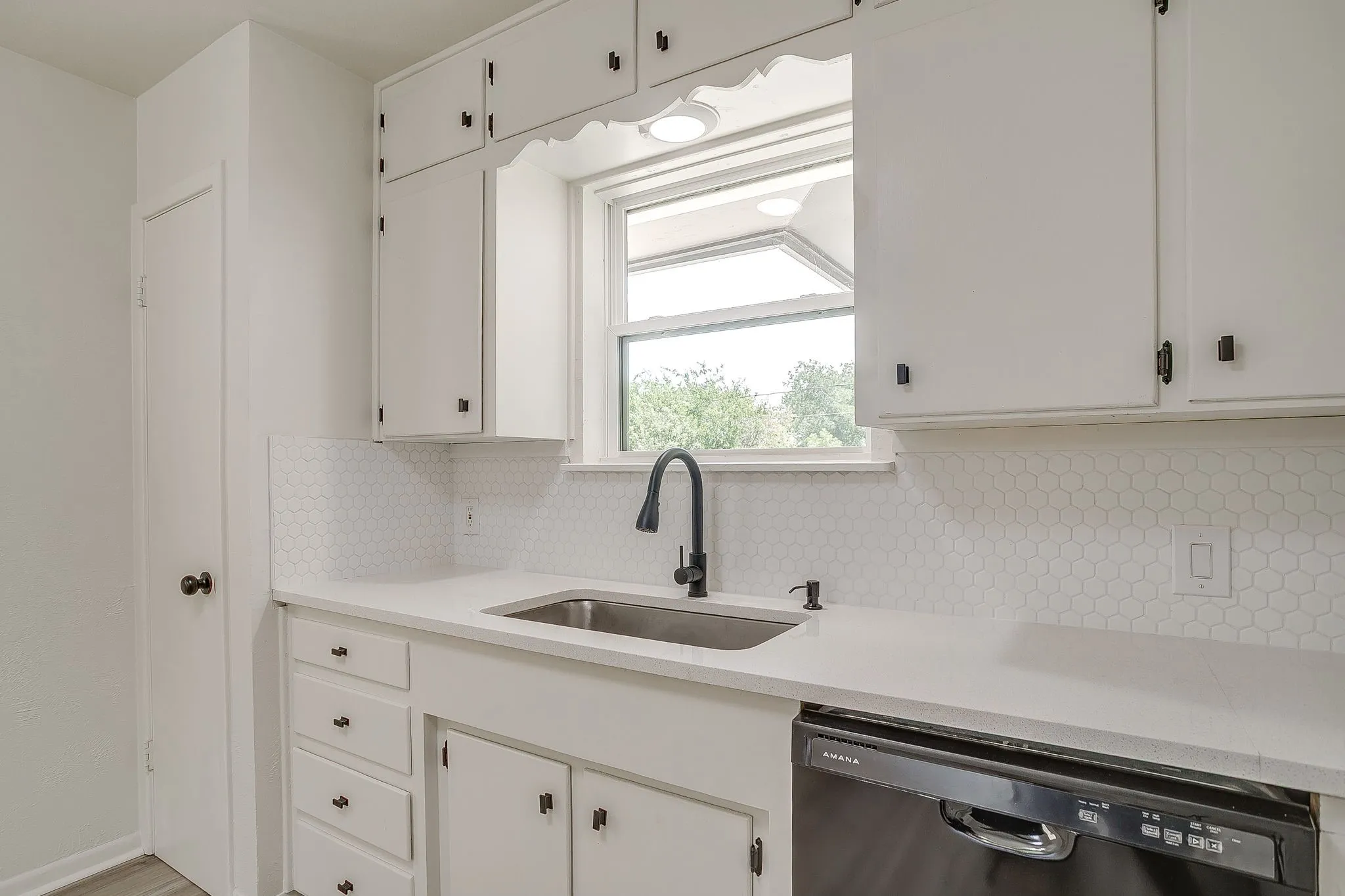 Kitchen space featuring white cabinetry, a stainless steel sink with a matte black faucet, and a hexagonal tile backsplash