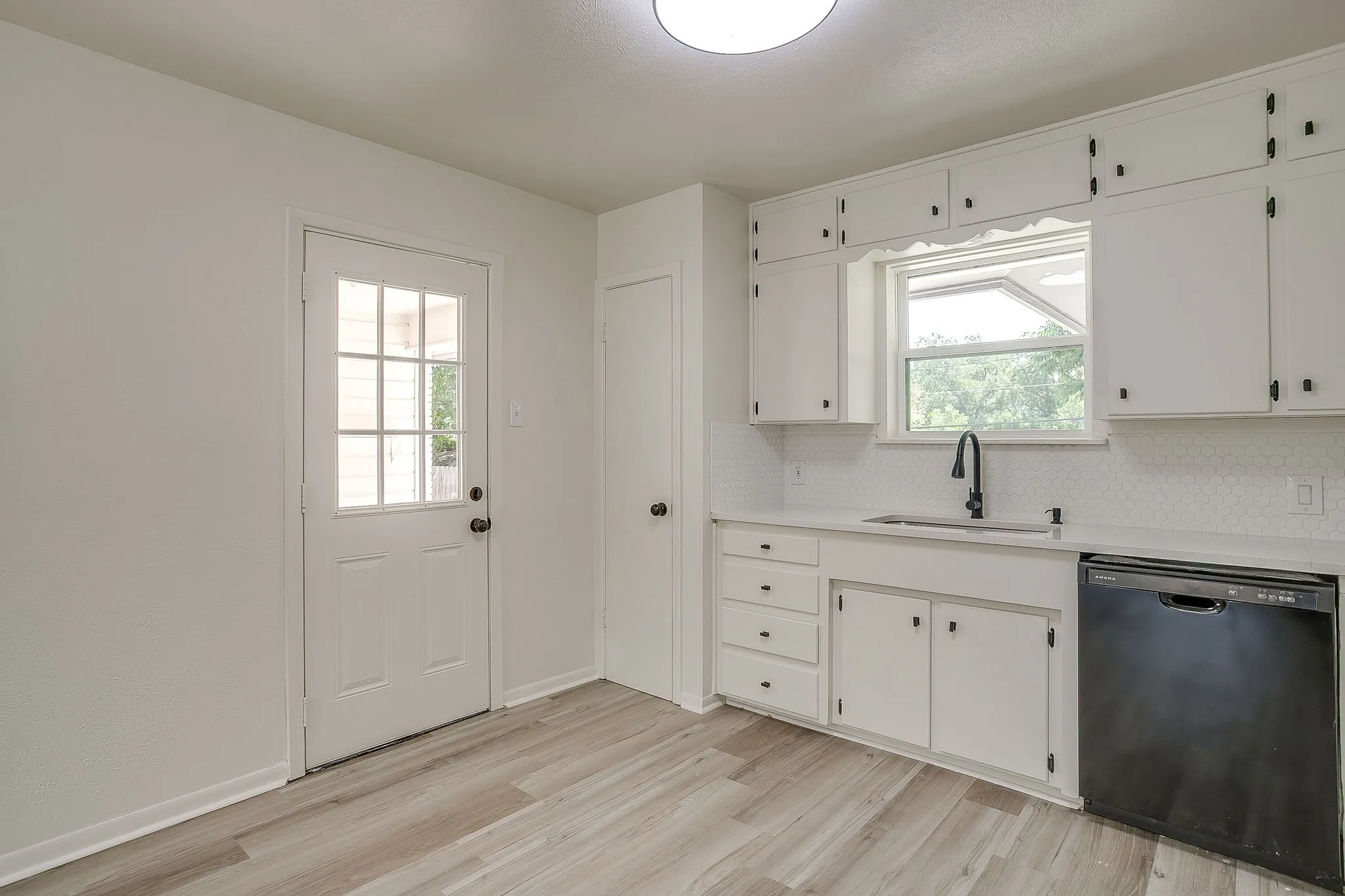 Kitchen featuring white cabinetry, light countertops, white mosaic tile backsplash, black dishwasher, and wood-finish flooring