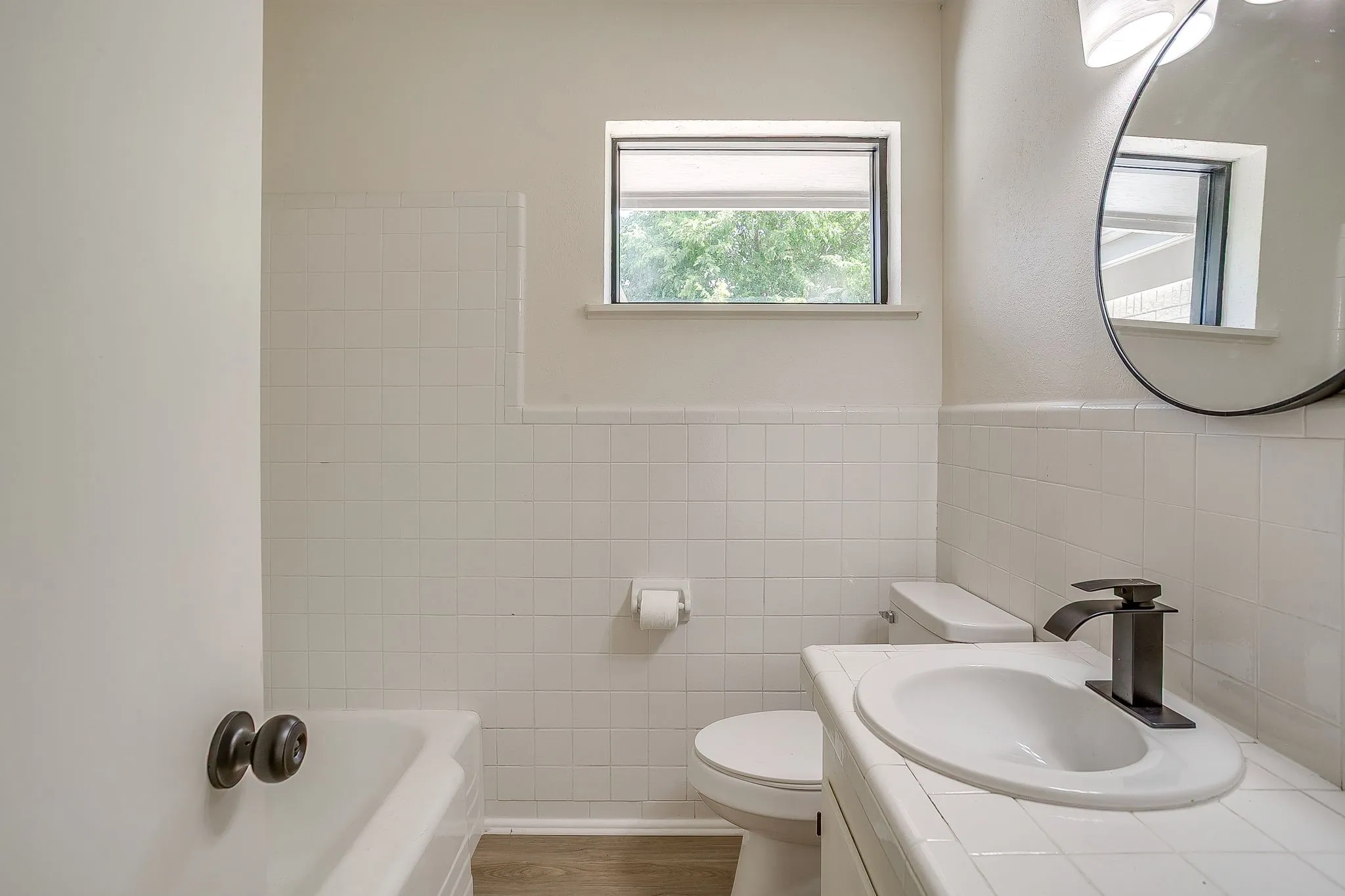 Bathroom featuring a white tile wainscoting, a rectangular window, and a wood-finish floor