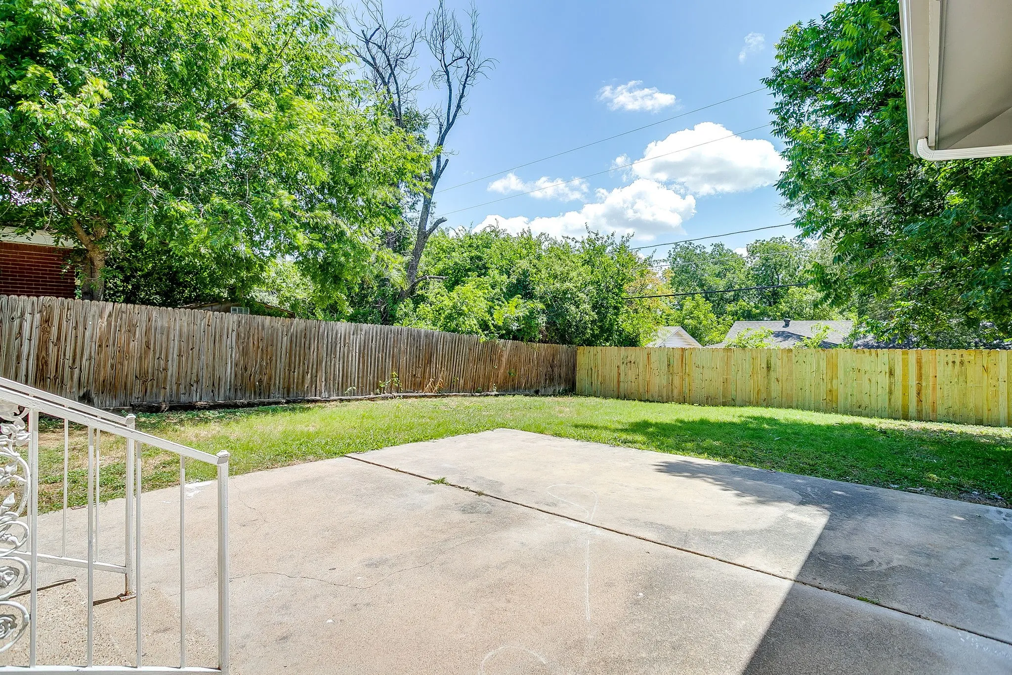 Expansive backyard featuring a concrete patio, a manicured lawn, and wood privacy fencing