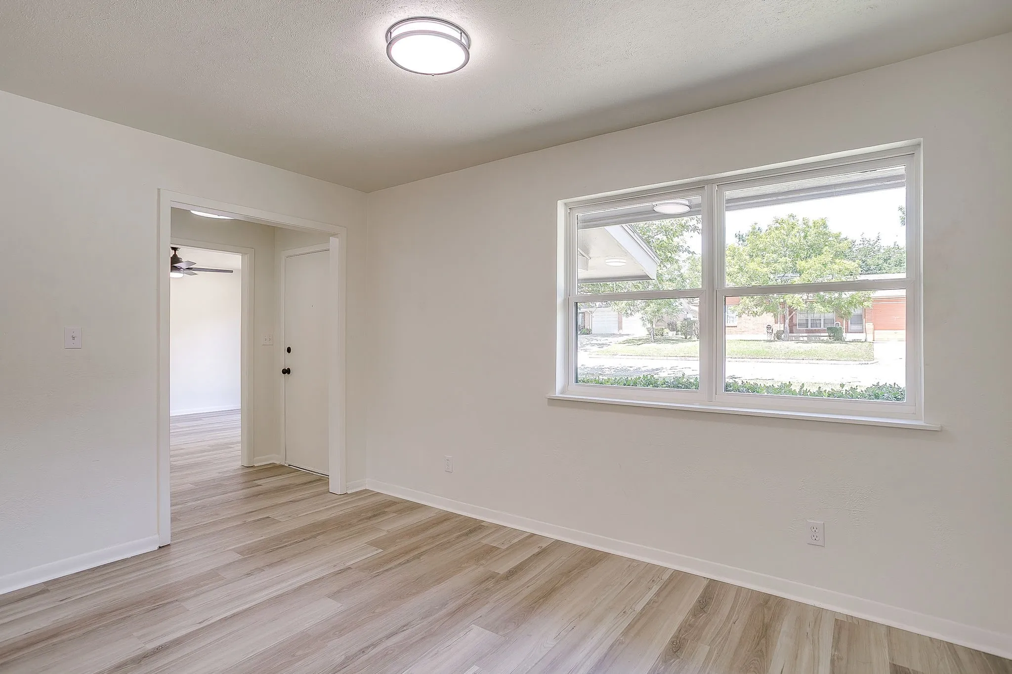 Bright room featuring wood-finish flooring, a contemporary flush-mount ceiling light, and a large multi-pane window