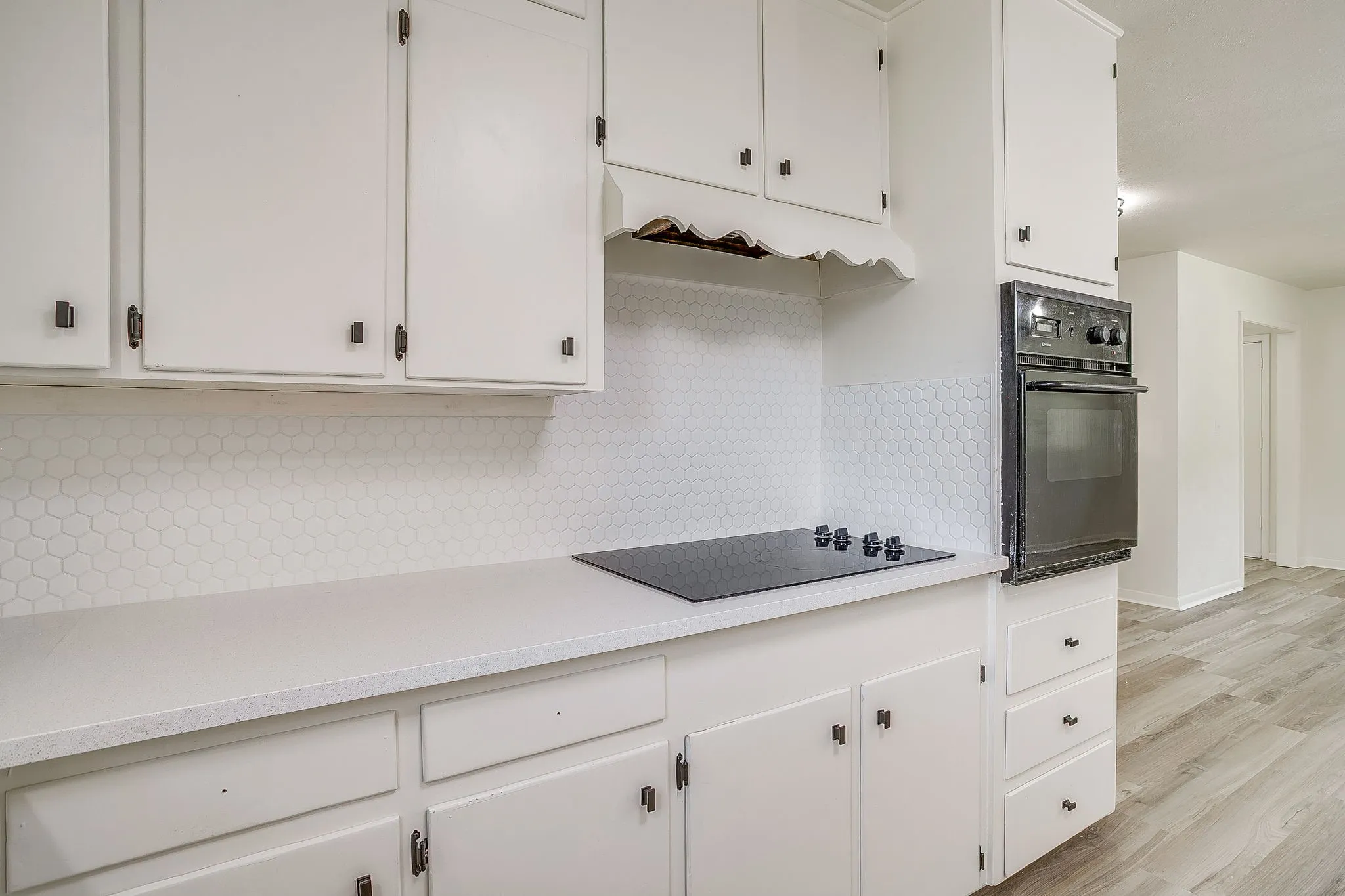 Kitchen featuring white cabinetry, a built-in wall oven, a black electric cooktop, light-toned countertops, and a white hexagonal tile backsplash