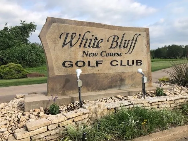 Golf club entrance featuring a stone-look sign with raised lettering, an integrated concrete base, and stone retaining walls
