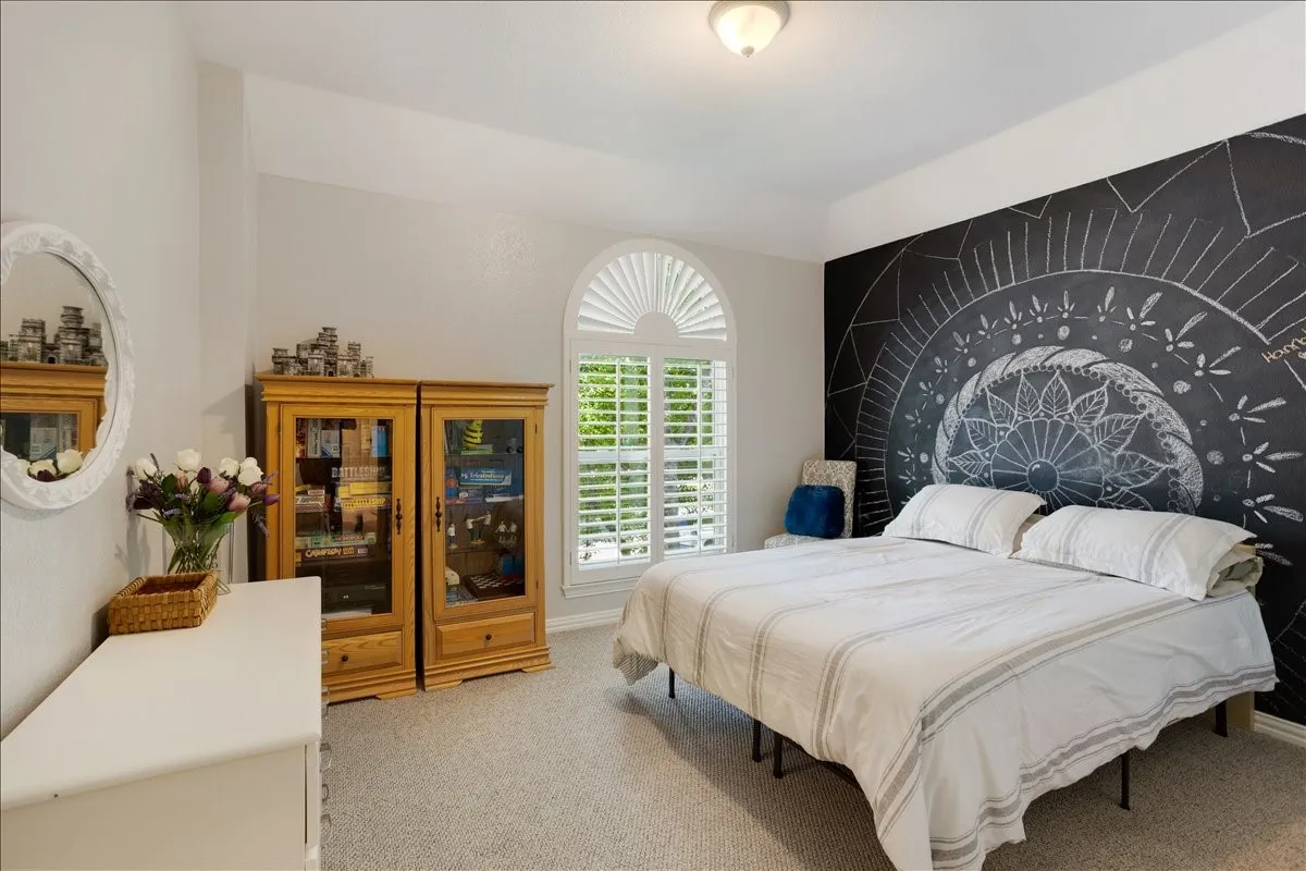 Bedroom featuring a statement chalkboard wall, arched window with plantation shutters, light gray wall paint, and recessed ceiling lighting
