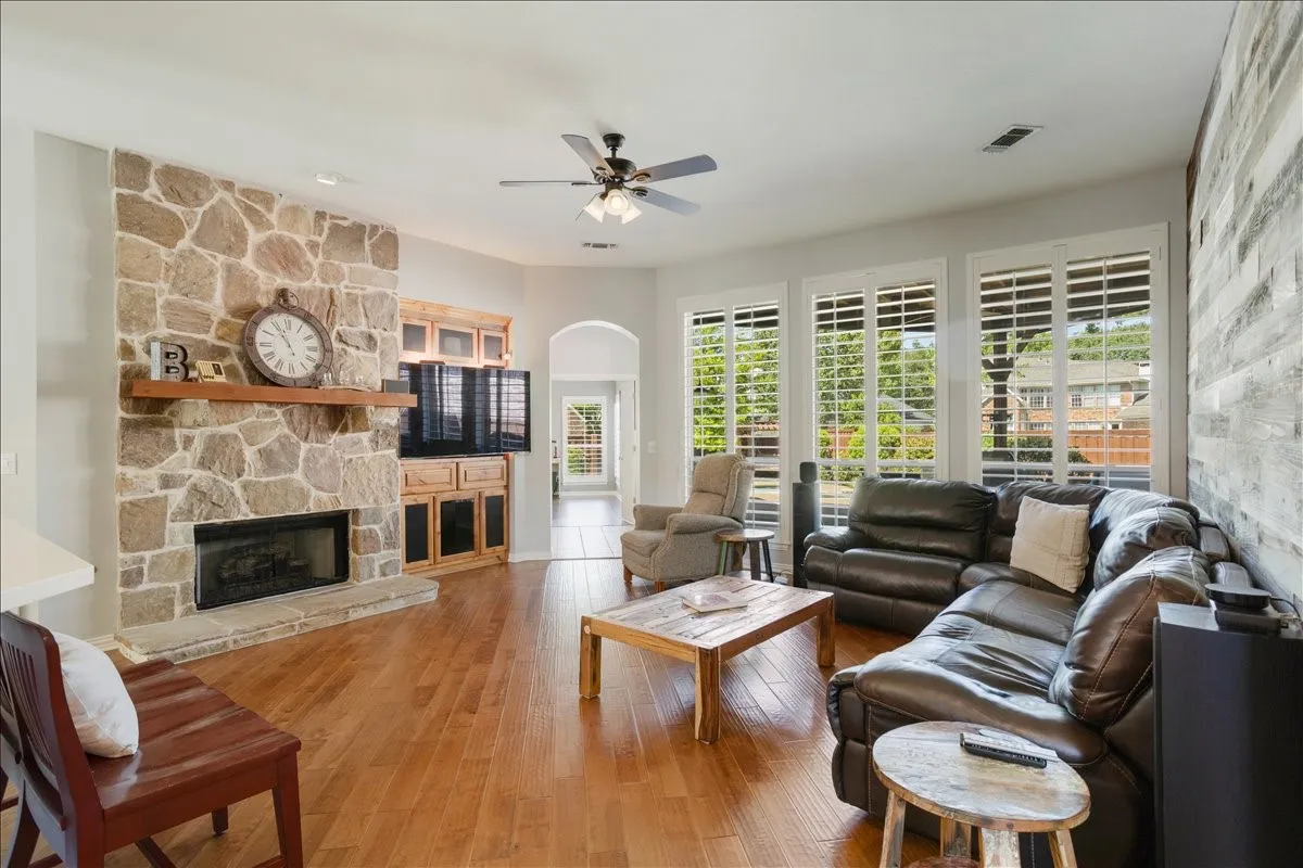 Living area featuring wood-finish flooring, a stone-faced fireplace with a wood mantle, and a built-in media cabinet