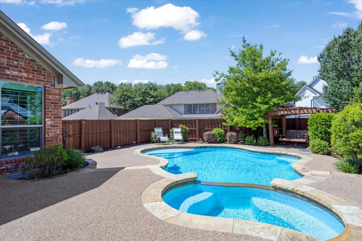 Brick exterior featuring a multi-level swimming pool with integrated spa, bordered by natural stone coping and a surrounding aggregate patio