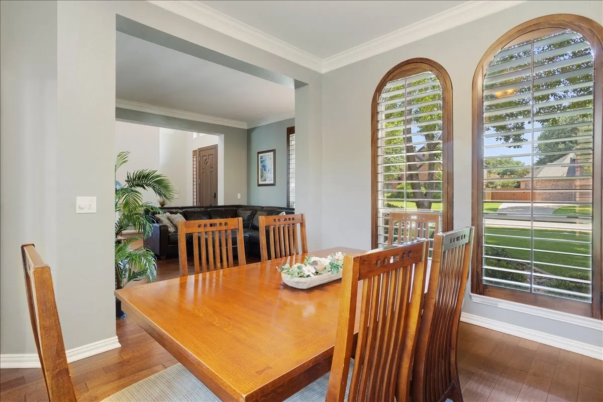 Dining area featuring wood-finish flooring, crown molding, and two arched windows with plantation shutters