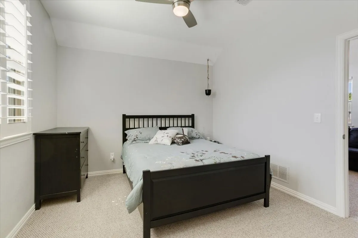 Carpeted room featuring a window with white plantation shutters, a sloped ceiling, and a ceiling fan with integrated lighting