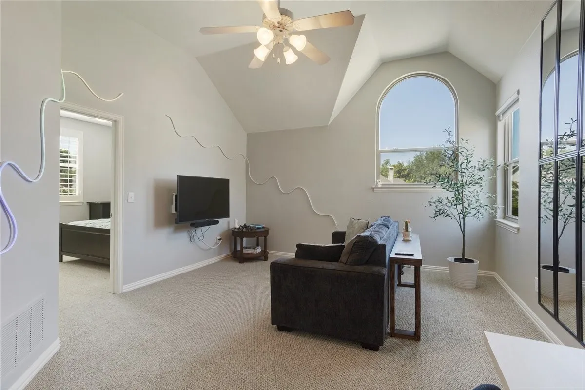 Carpeted bonus room featuring a vaulted ceiling with a ceiling fan, an arched window, and an additional window