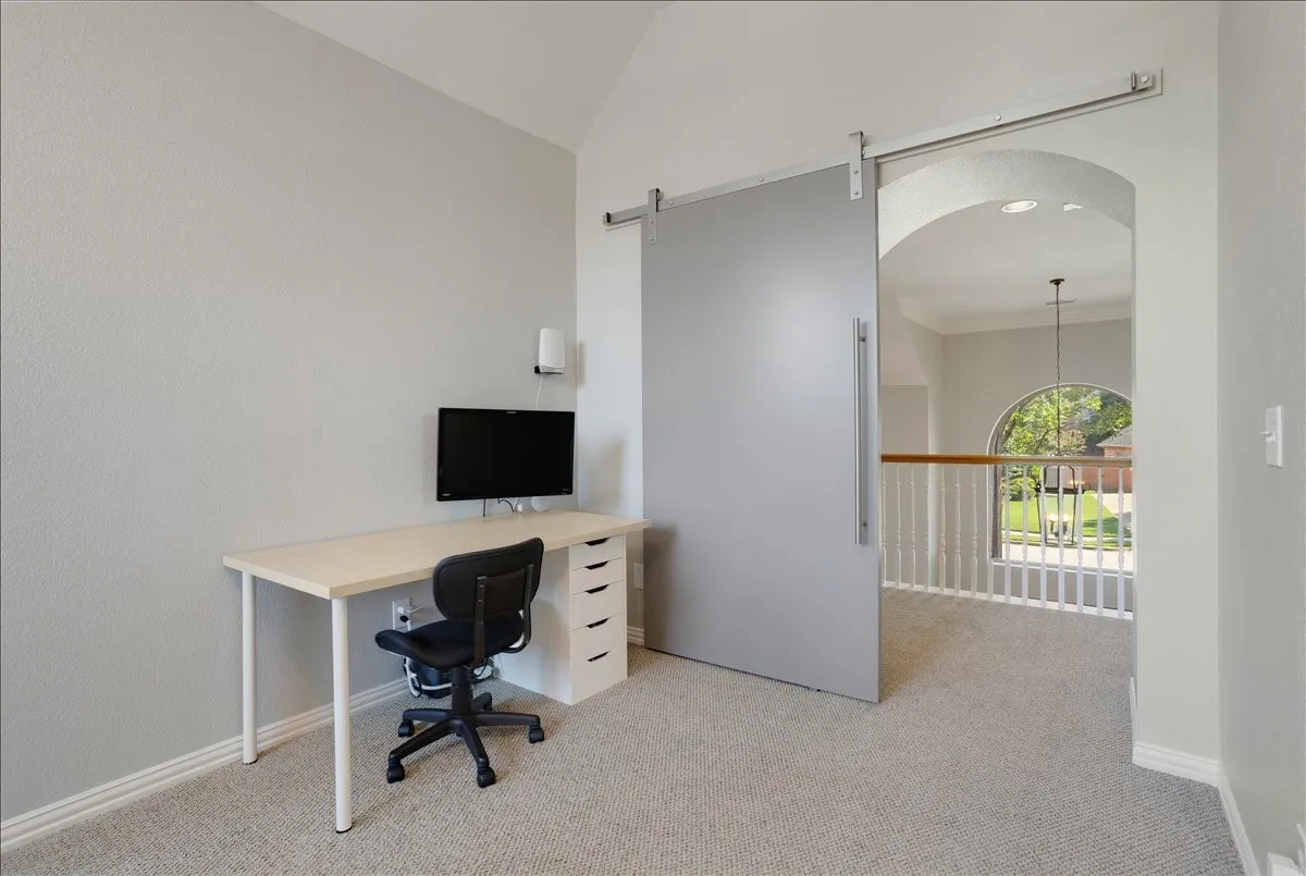 Carpeted loft area featuring a modern barn door with a horizontal pull, vaulted ceiling, and an arched window providing natural light