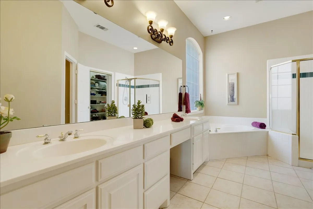 Spacious bathroom featuring a dual vanity with integrated sinks, a built-in garden tub, a separate corner shower with glass enclosure, an arched window, and tile flooring