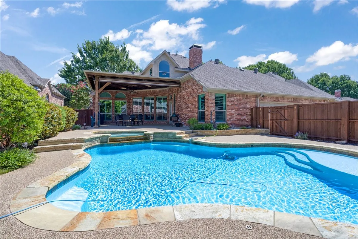 Inviting backyard oasis featuring a custom-shaped swimming pool with integrated spa, stone coping, and a textured concrete deck
