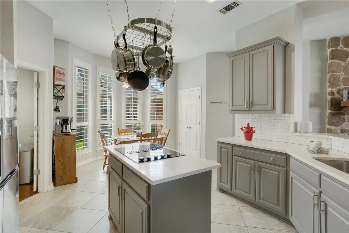 Kitchen featuring a central island with an integrated cooktop, light gray cabinetry, white countertops, and a white subway tile backsplash