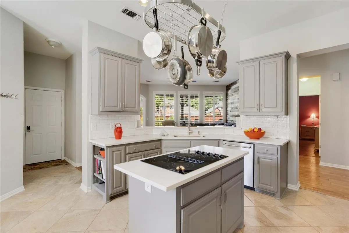 Kitchen featuring a central island with an integrated cooktop, light gray cabinetry, white countertops, and a white subway tile backsplash