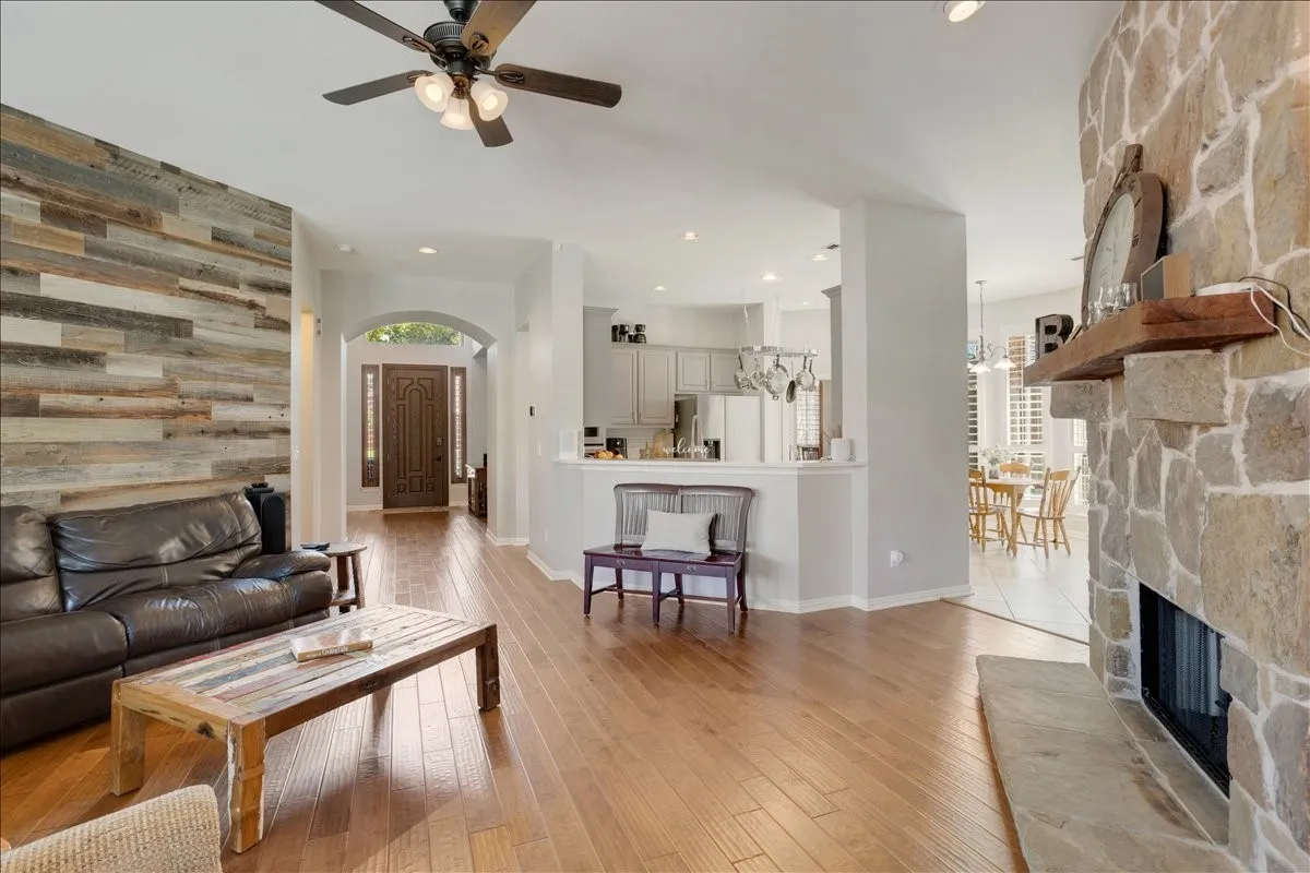 Living area featuring wood-finish flooring, a stone fireplace with a wood mantel, a feature wall with horizontal wood planks, and a ceiling fan