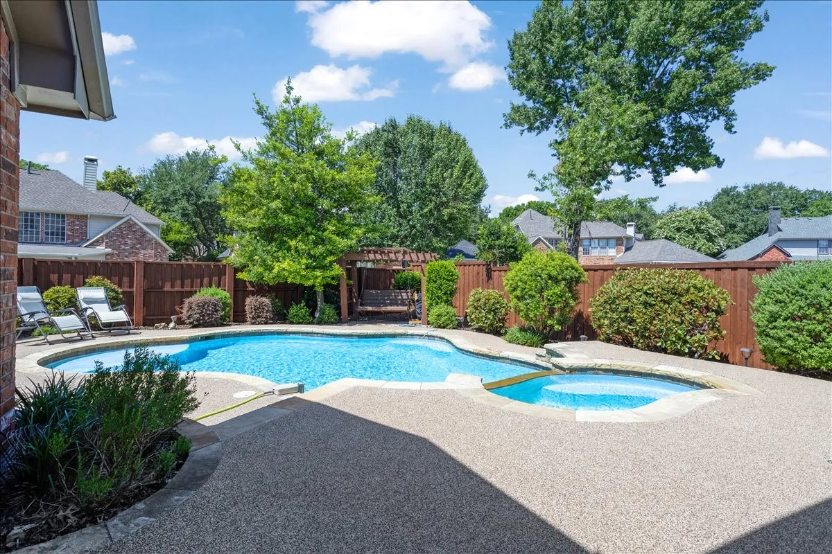 Resort-style backyard featuring a freeform swimming pool, integrated spa, and expansive exposed aggregate patio