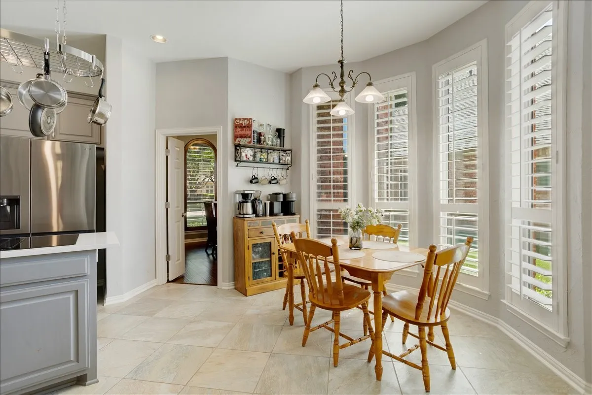 Kitchen dining area featuring a bay window with plantation shutters, tile flooring, recessed lighting, and a pot rack system