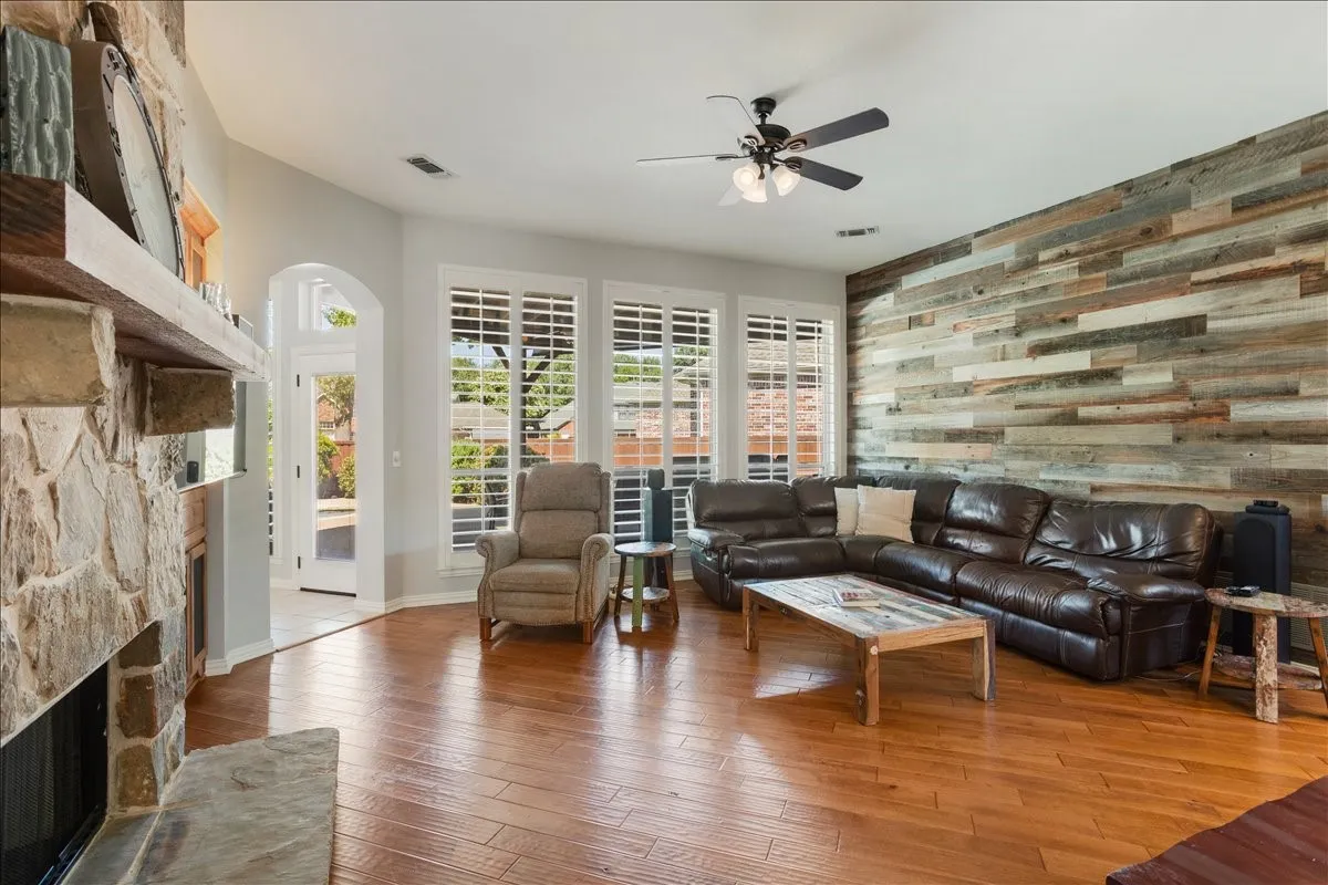 Spacious living area featuring wood-finish flooring, a full-height stone fireplace with a substantial mantel, and a distinctive wood plank accent wall