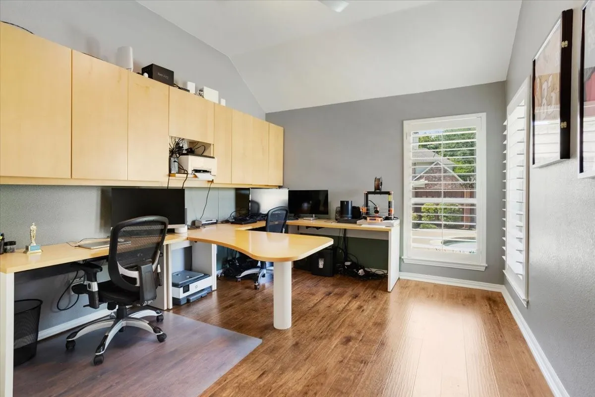 Dedicated office space featuring extensive built-in cabinetry, wood-finish flooring, and a vaulted ceiling