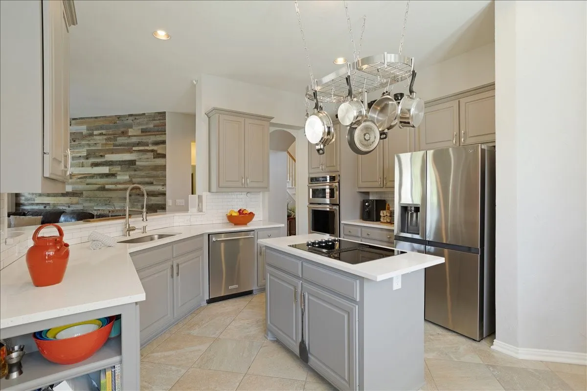 Kitchen featuring light gray cabinetry, stainless steel appliances, a center island with a cooktop, white countertops, and a subway tile backsplash