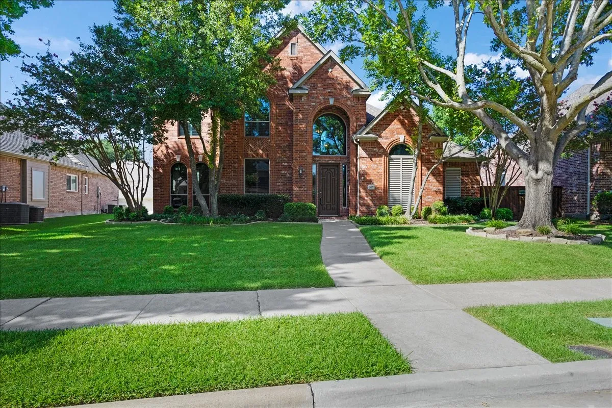 Traditional brick exterior featuring a prominent arched window, mature trees, a concrete walkway, and a manicured lawn