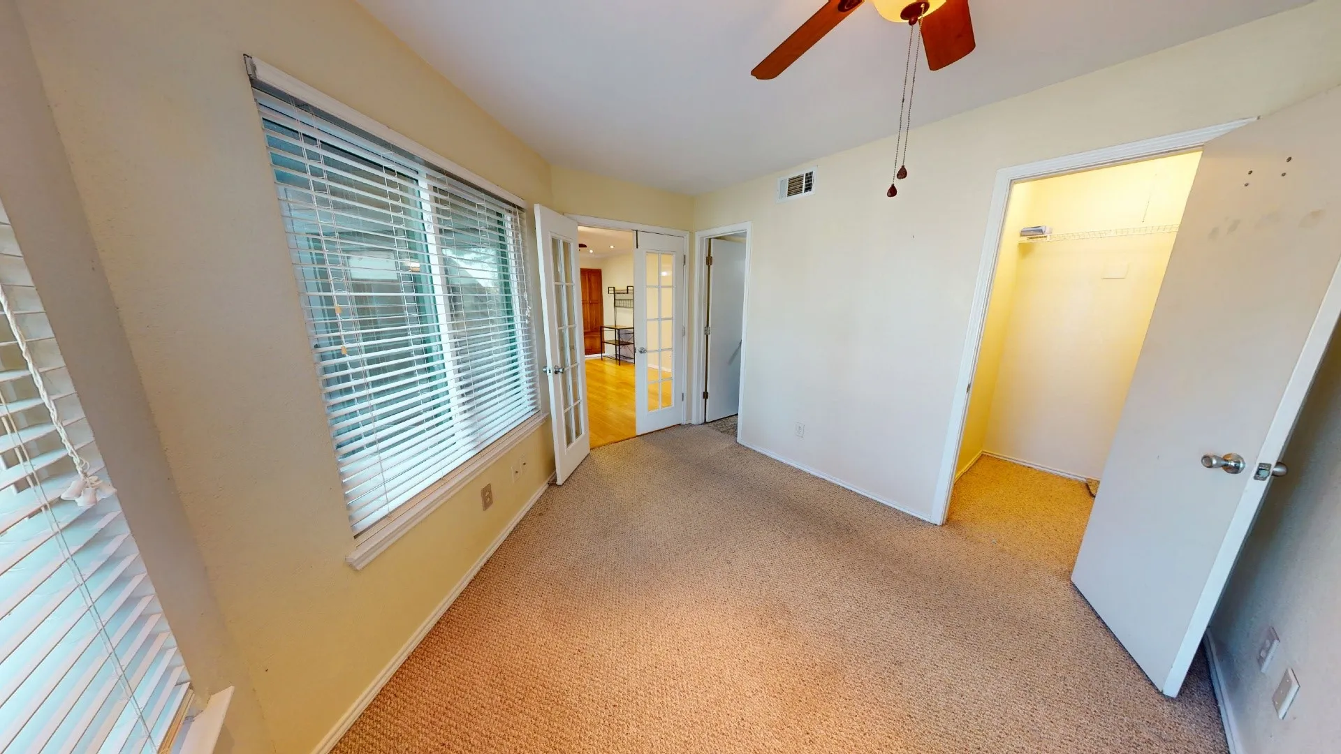 Carpeted room featuring a large window with blinds, a ceiling fan, and a built-in closet with shelving