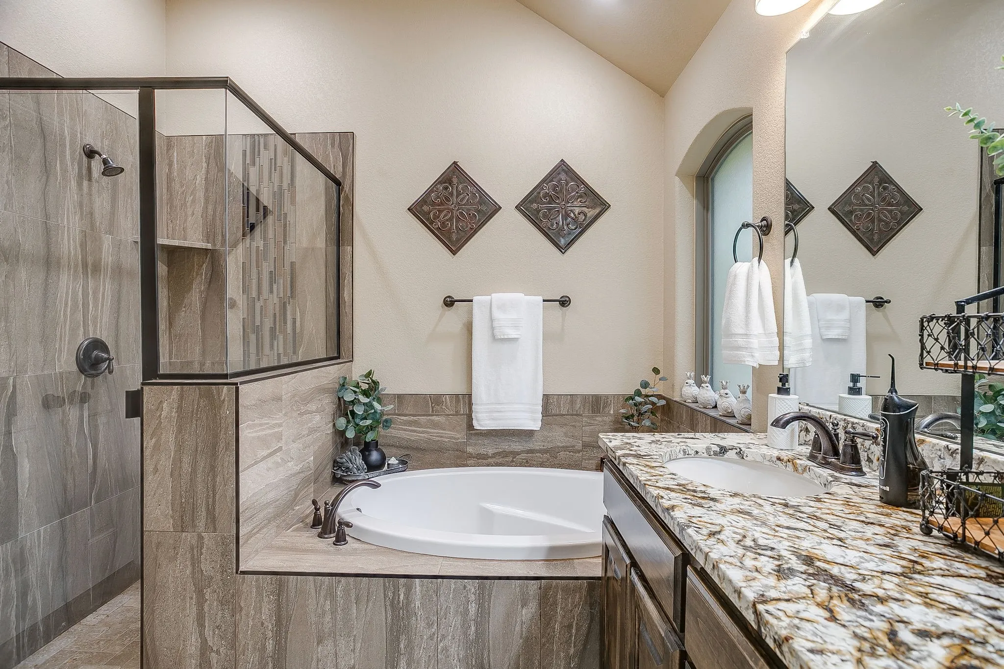 Bathroom featuring a built-in soaking tub, a walk-in shower with glass enclosure, a single vanity with stone countertop, and an arched window