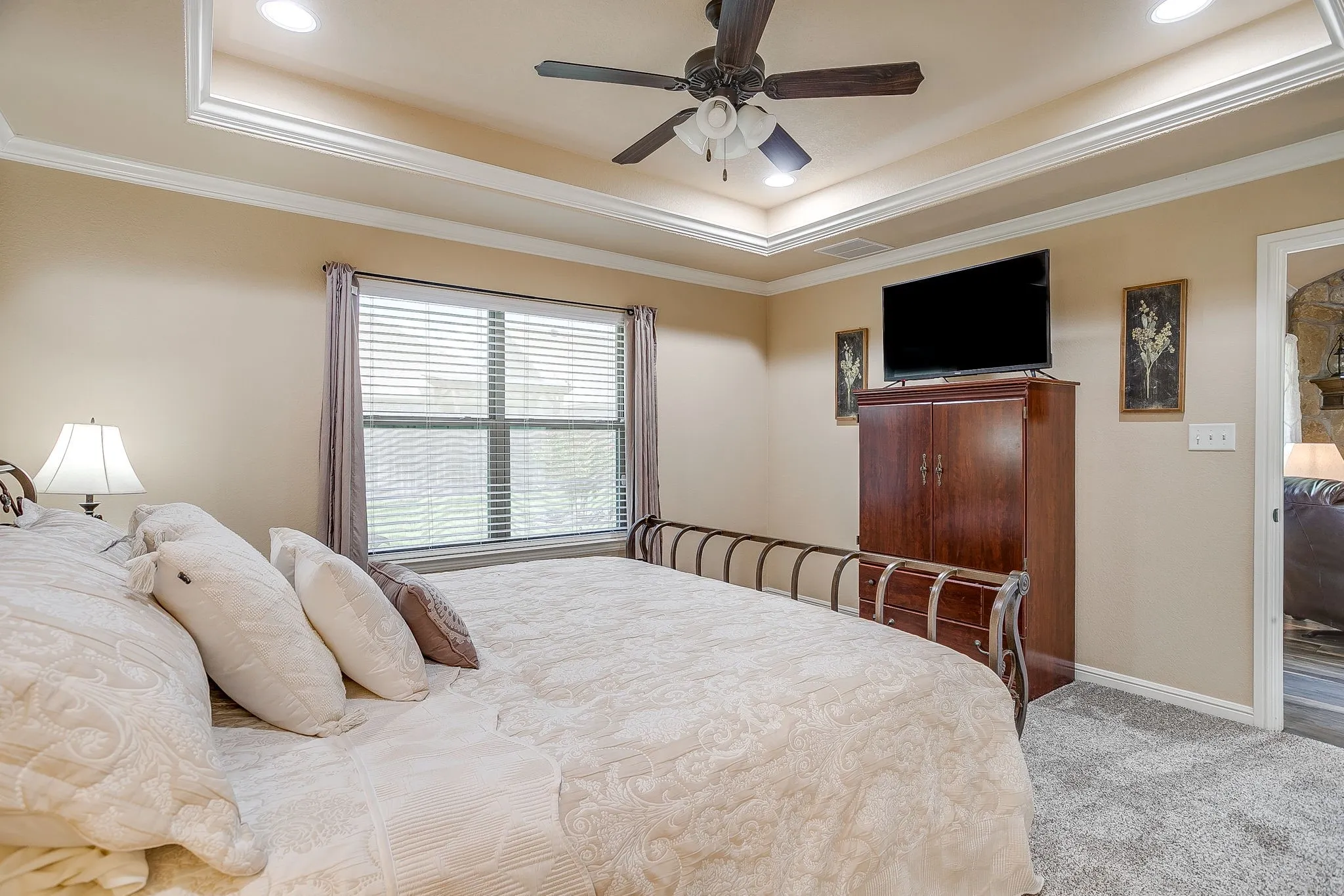 Spacious bedroom featuring neutral wall tones, tray ceiling with recessed lighting and a ceiling fan, window with blinds and draperies, and plush carpeting