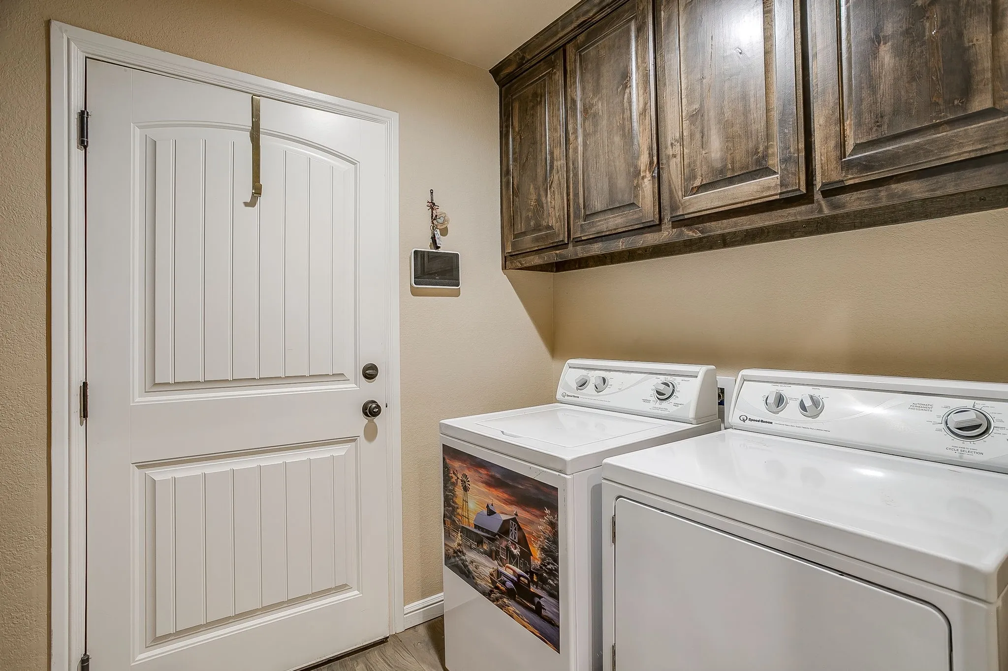 Laundry area featuring wood-finish flooring and upper cabinetry with dark wood-finish doors