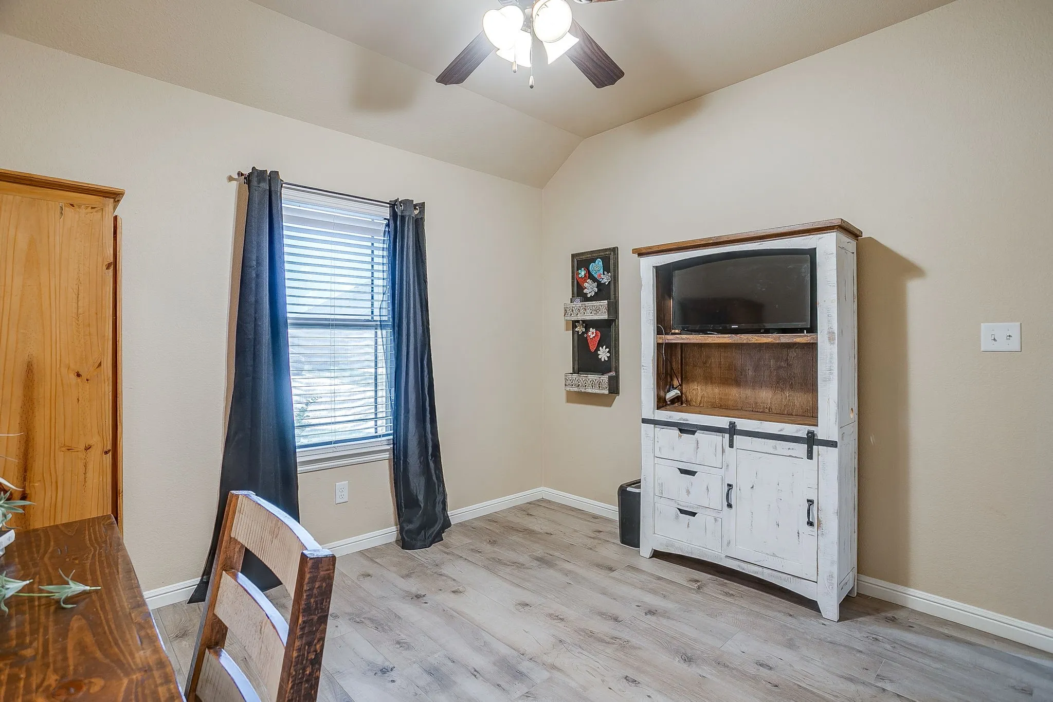 Interior space featuring a vaulted ceiling with a ceiling fan, wood-finish flooring, and a window with horizontal blinds