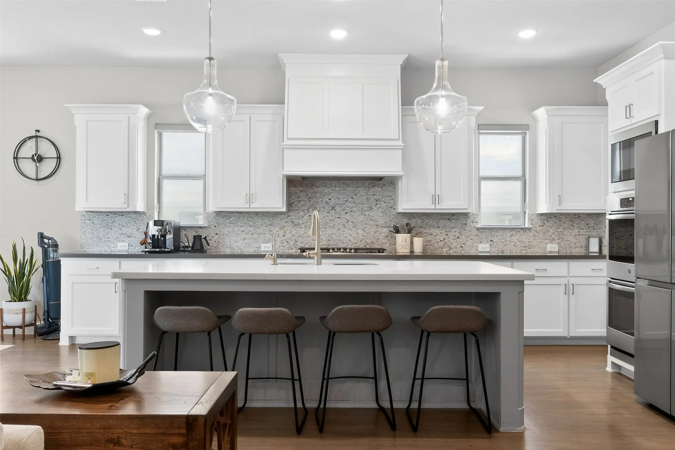 Modern kitchen featuring a large central island with seating, white shaker cabinetry, stainless steel appliances, pendant lighting, and mosaic tile backsplash