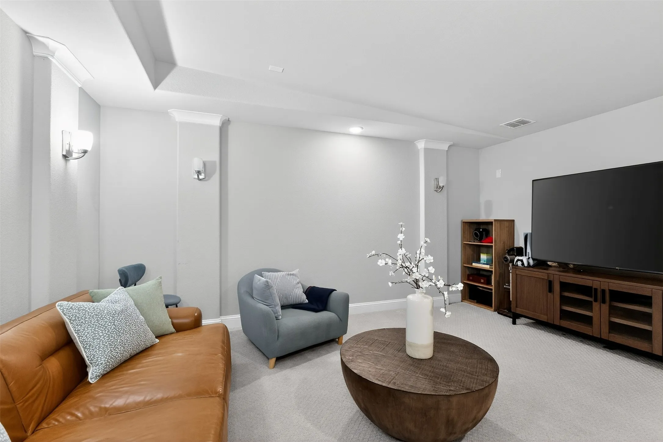 Recessed lighting and wall sconces illuminate this living area featuring crown molding and a tray ceiling