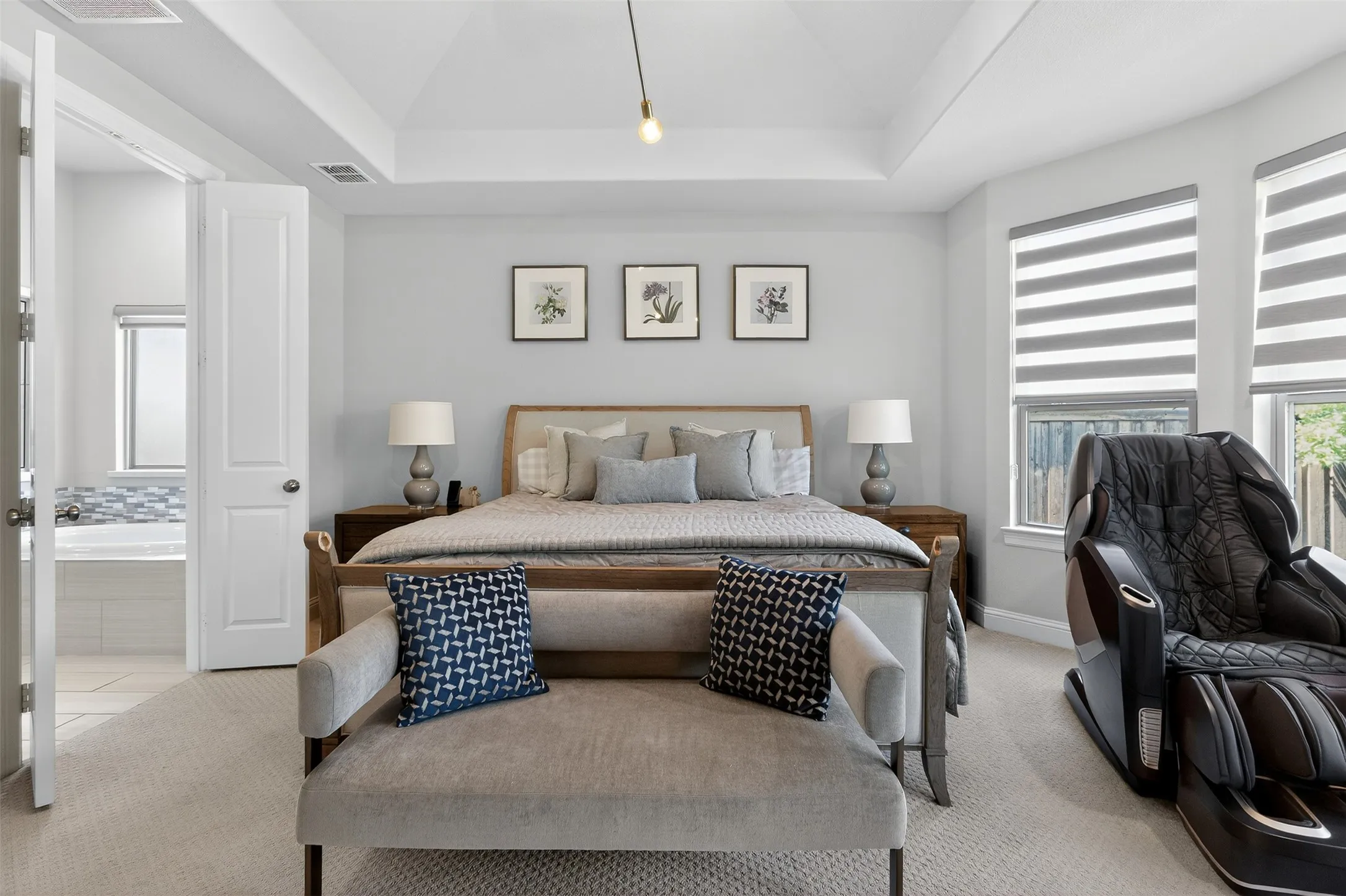 Bedroom featuring a tray ceiling with pendant lighting, dual windows with banded shades, and carpet flooring
