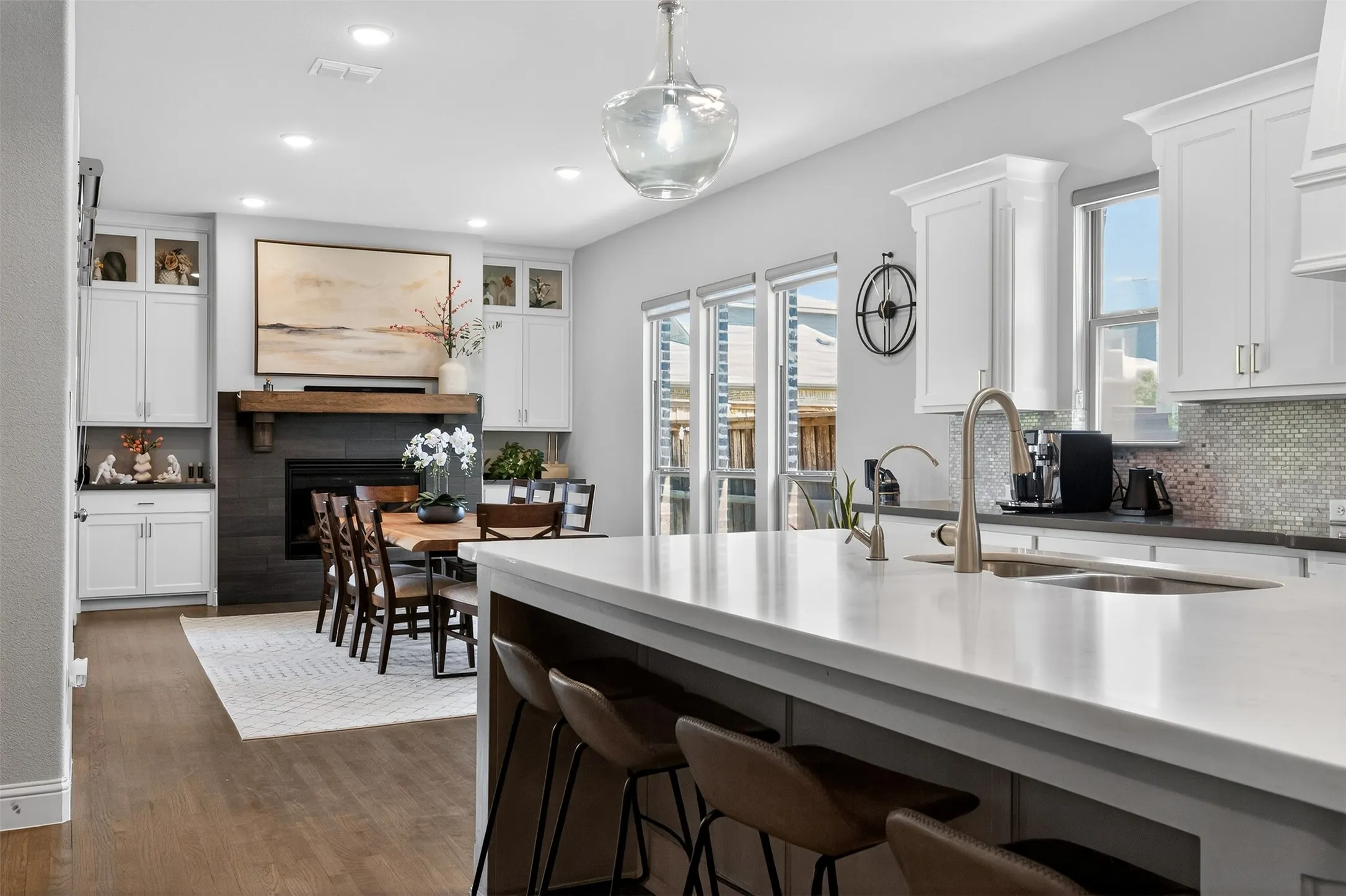 Open-concept kitchen and dining area featuring a large island with seating, a fireplace with a wood mantle, white cabinetry, recessed lighting, and wood-finish flooring