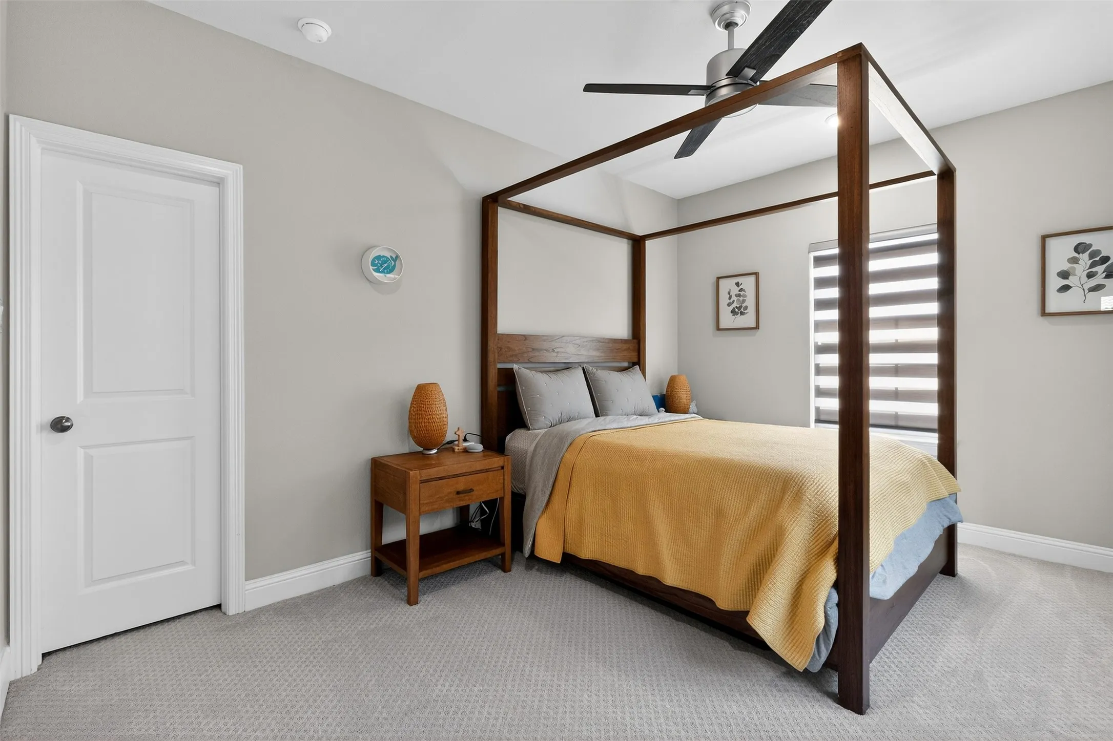Spacious room featuring light gray walls, textured gray carpeting, a contemporary ceiling fan, a window with horizontal blinds, and a white interior door with dark hardware
