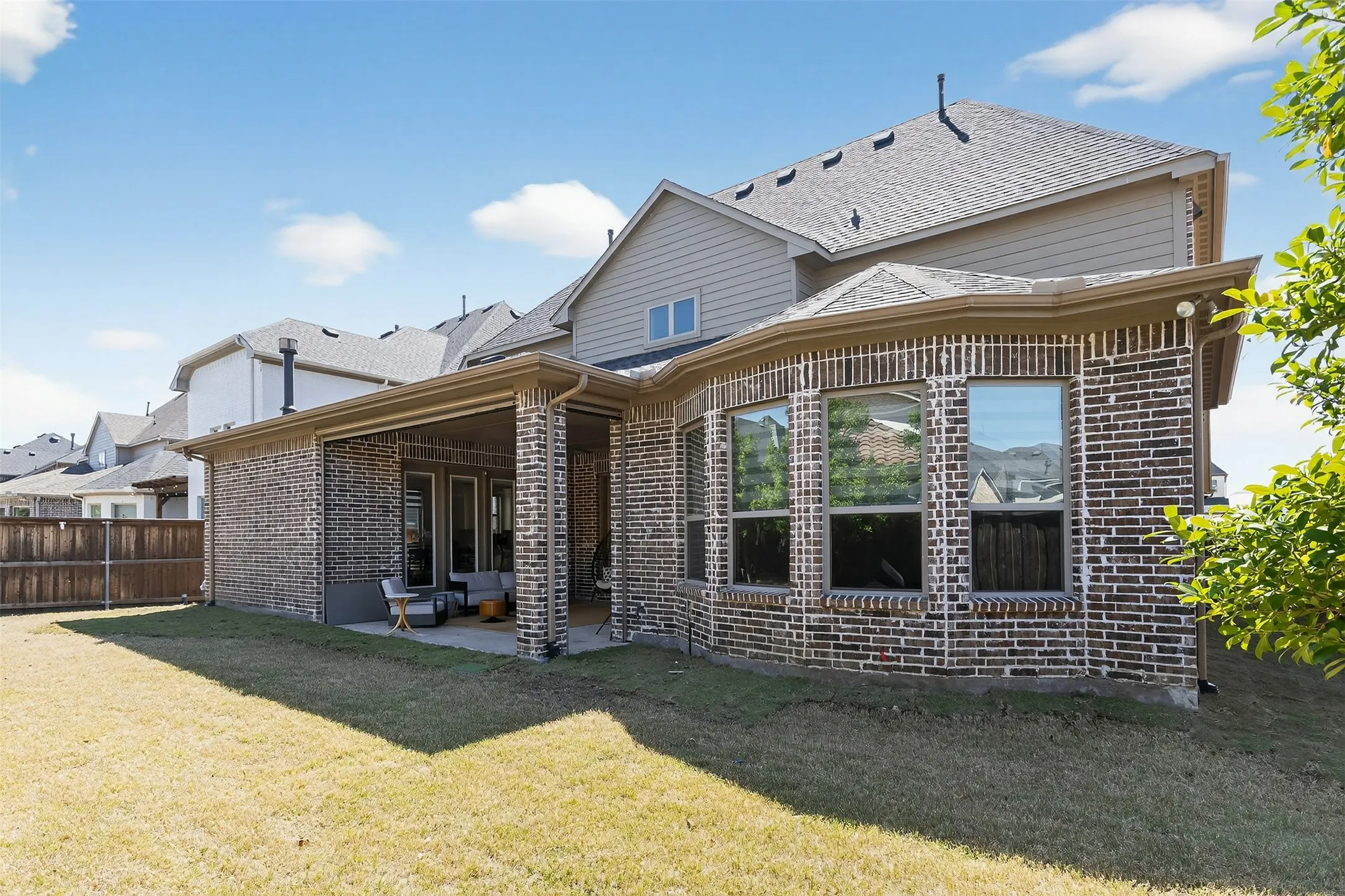 Expansive backyard featuring a covered patio with a concrete slab, multiple large windows, and a combination of brick and siding exterior