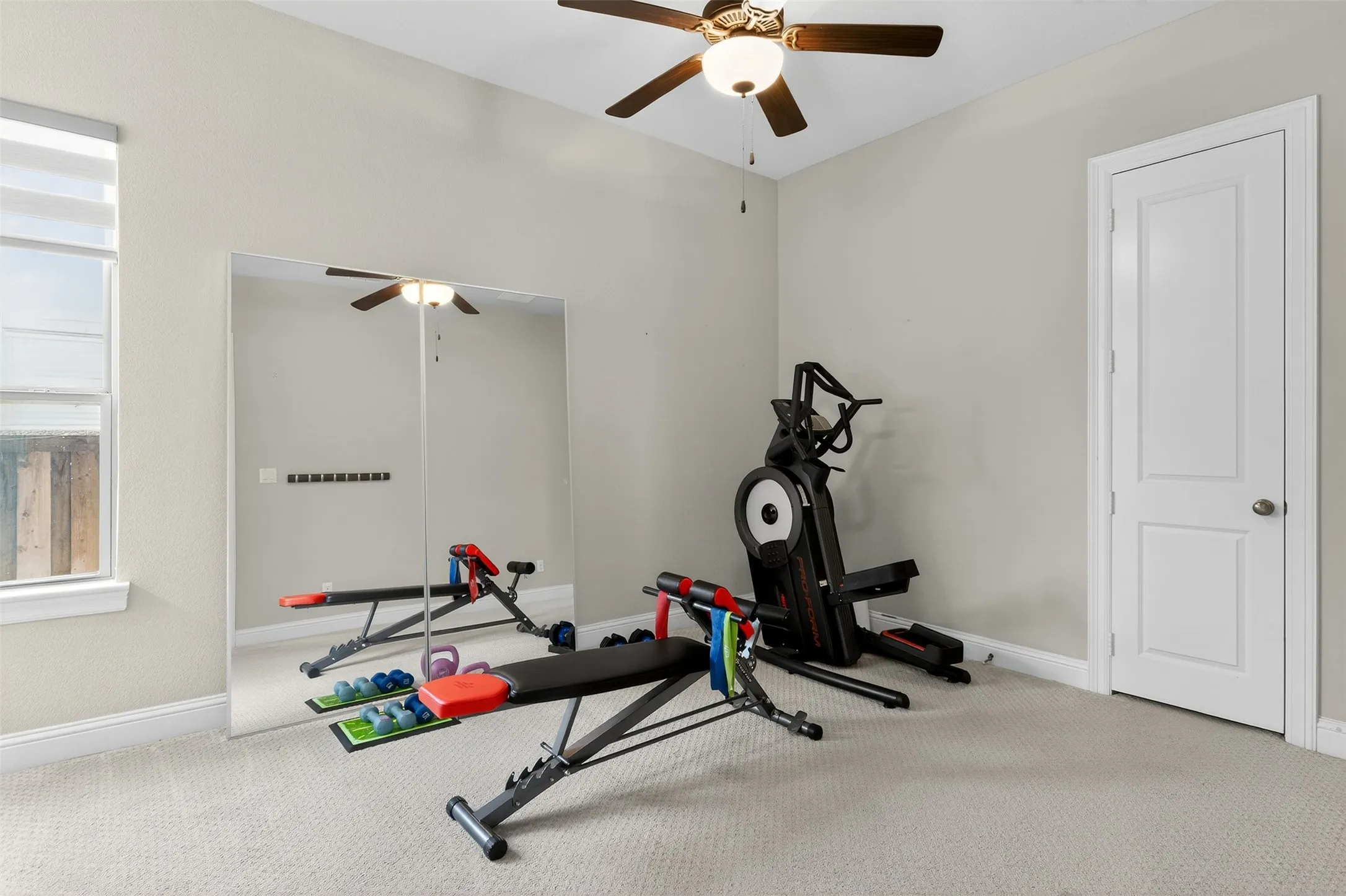 Versatile room featuring light neutral wall paint, soft carpet flooring, a large full-wall mirror, and a ceiling fan with integrated lighting