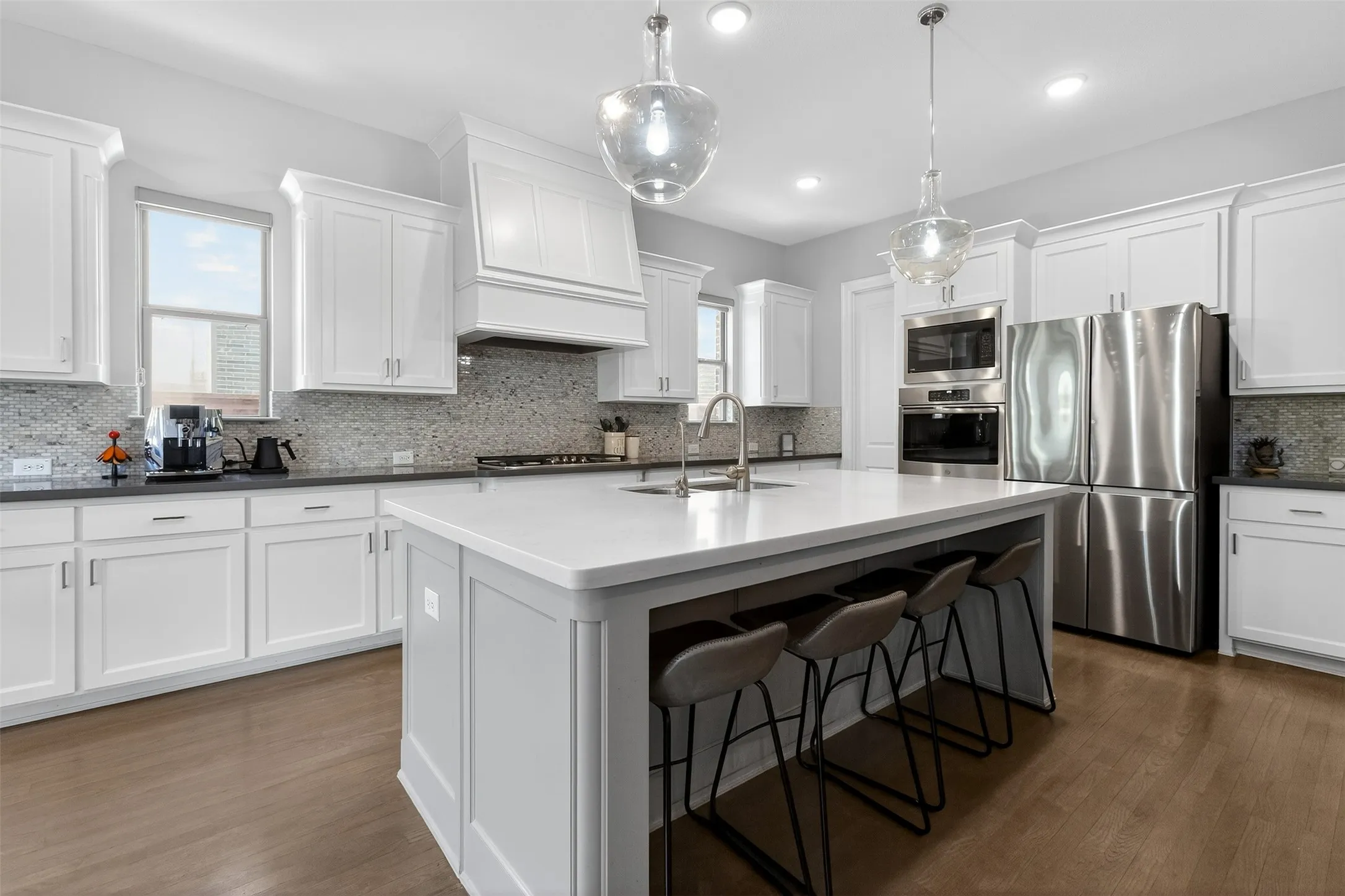 Bright kitchen featuring an expansive center island with seating, white shaker cabinetry, stainless steel appliances, and wood-finish flooring
