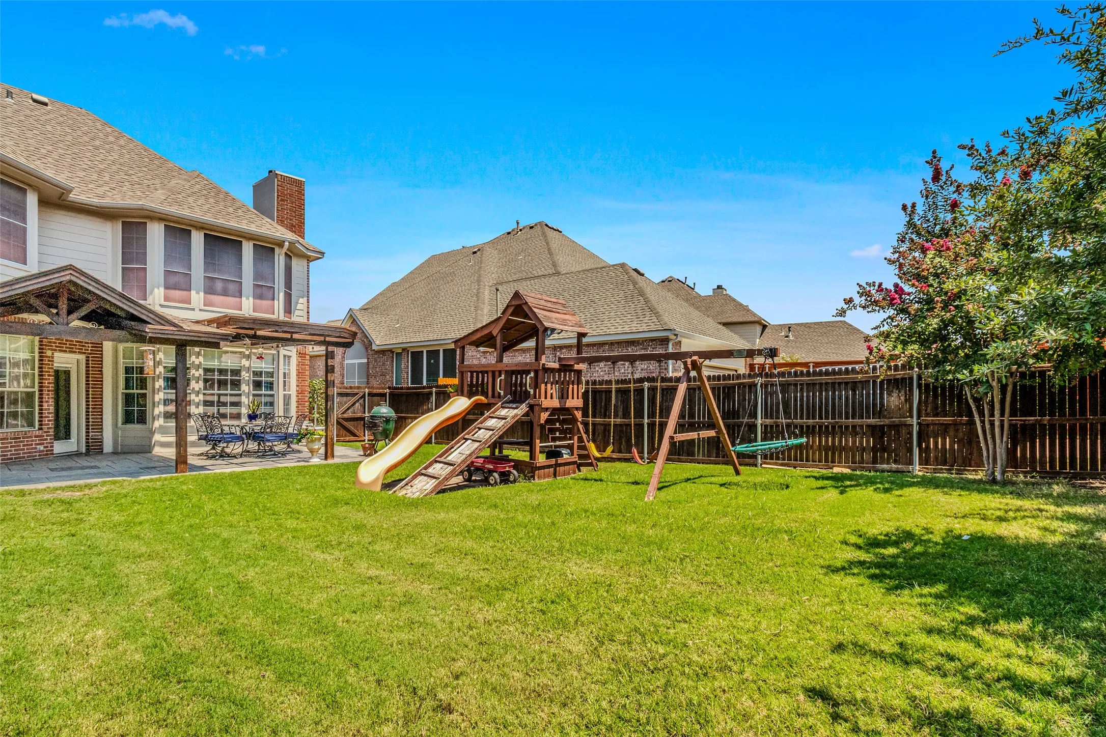 Expansive backyard featuring a lush lawn, a wood fence, and a patio area with a pergola