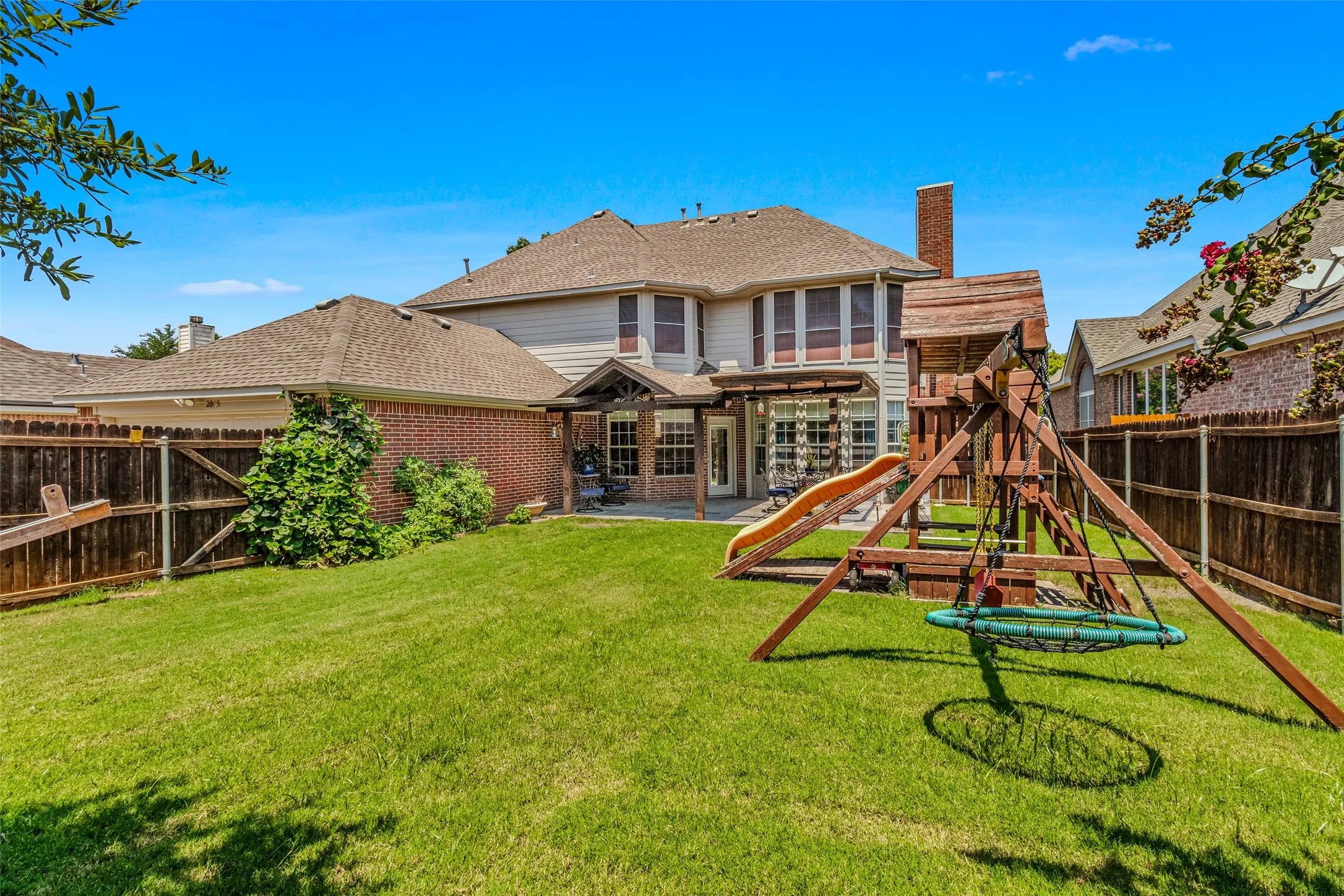 Expansive backyard featuring a manicured lawn, full privacy fencing, and a covered patio area