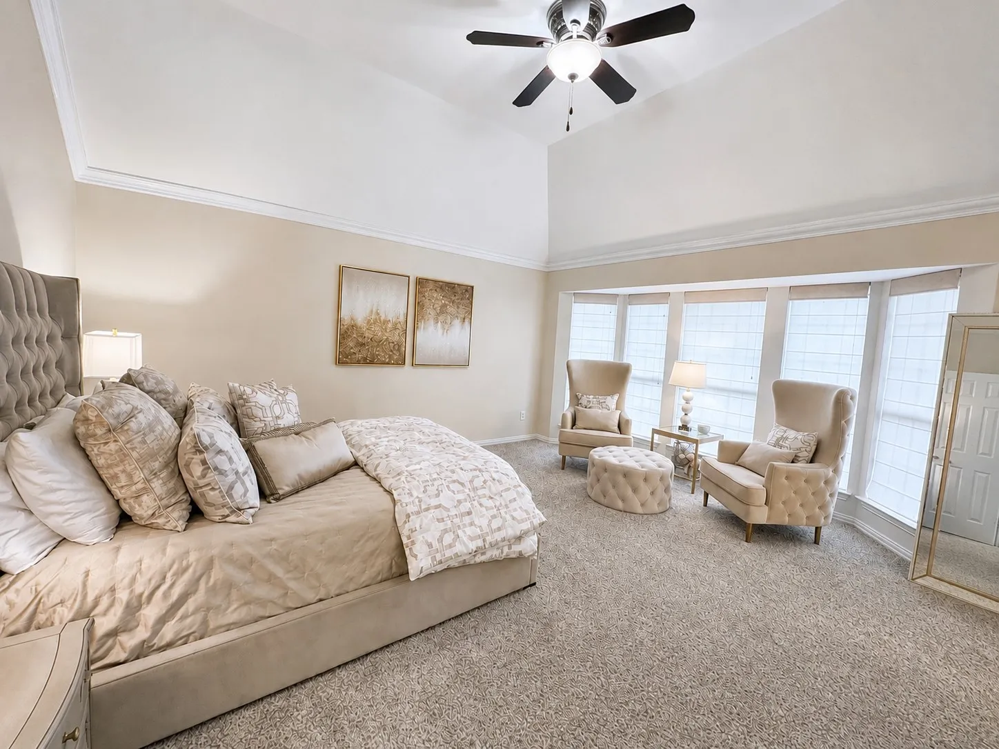 Vaulted ceiling with crown molding, ceiling fan, bay window with blinds, and neutral tone carpeting