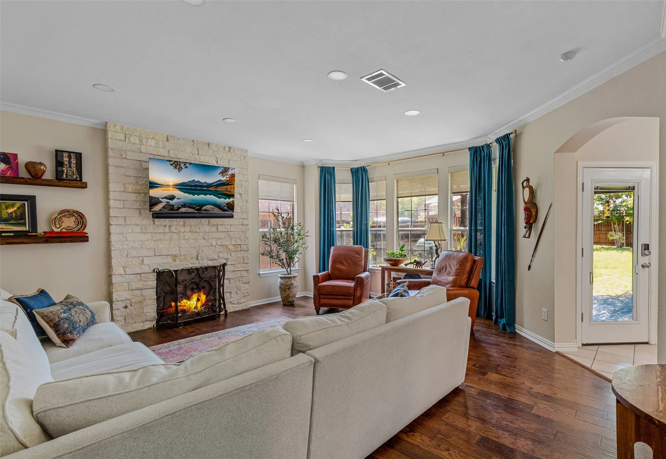Living area featuring a stone-clad fireplace, dark wood-finish flooring, recessed lighting, crown molding, and bay windows