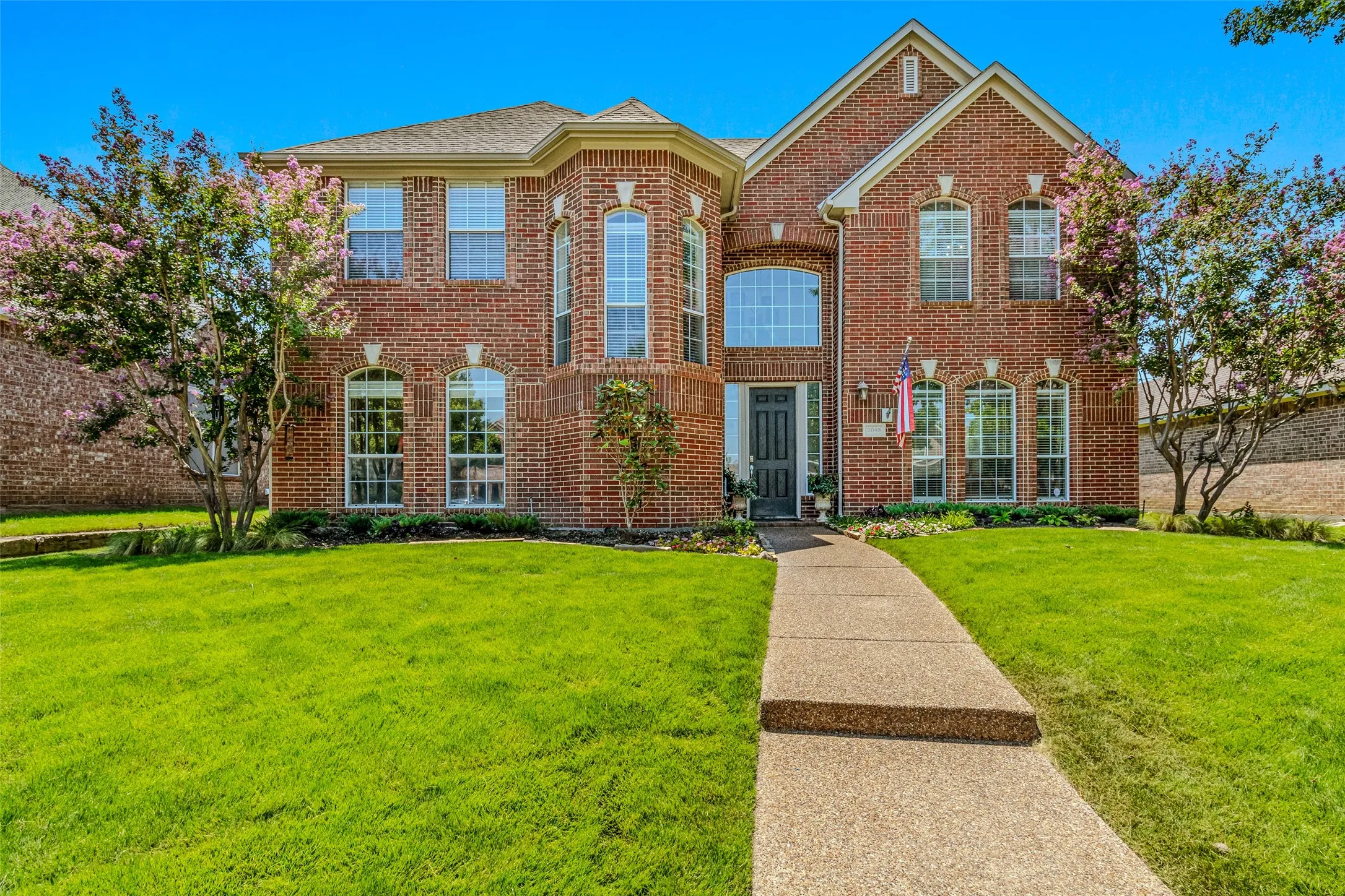 Two-story brick exterior featuring multiple arched windows, a prominent gable, a covered entryway, and a concrete pathway