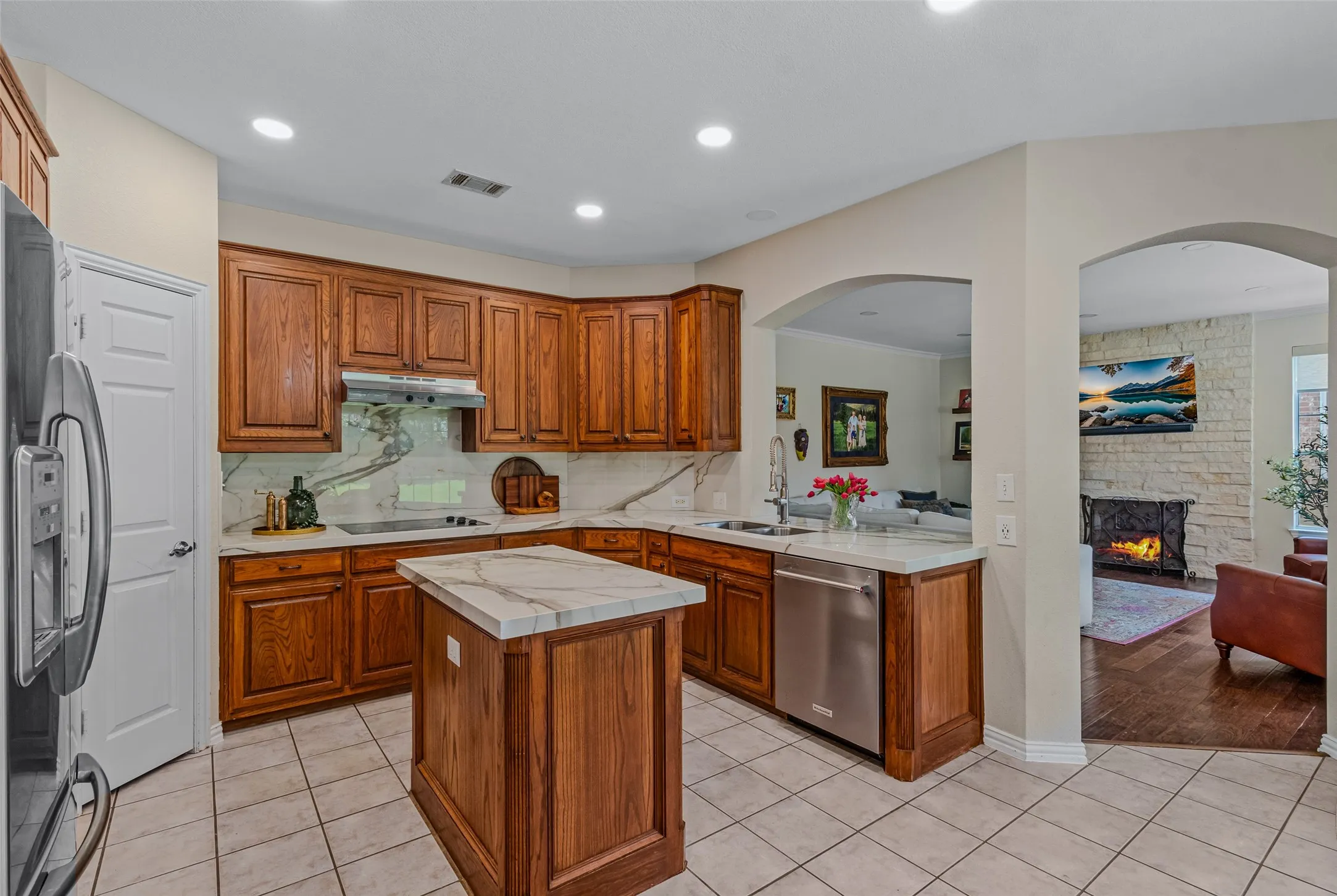 Kitchen featuring wood cabinetry, stone countertops with a matching backsplash, stainless steel appliances, and a central island