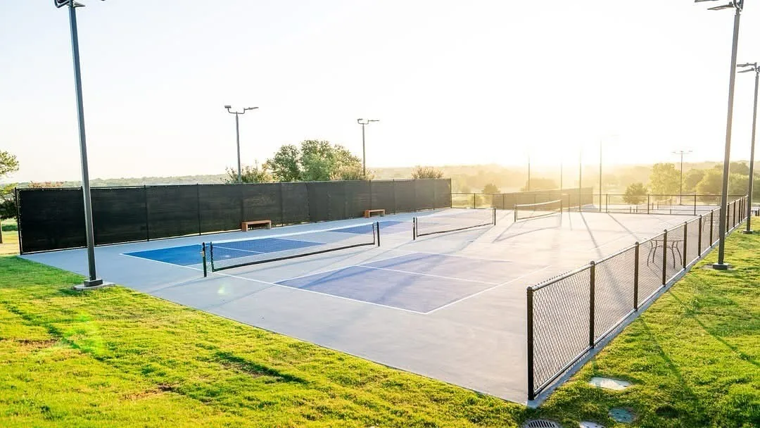 Multi-court facility featuring hard surface courts with painted blue and gray playing areas, perimeter fencing, and integrated lighting fixtures